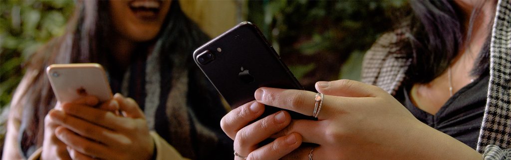 Two people using mobile phones with the phones being prominent in the photo.