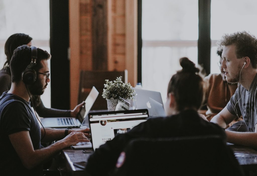 A group of people sitting around a table with laptops with headphones