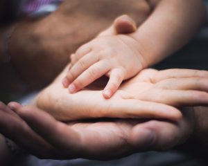 Two adult hands with a children's hand on top 