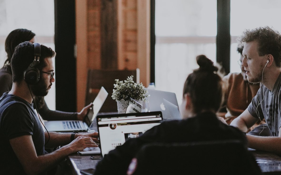 A group of people sitting around a table with laptops with headphones